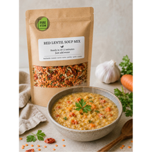 Load image into Gallery viewer, A kraft stand-up pouch of Pure KtoN Red Lentil Soup Mix stands next to a bowl of cooked lentil soup garnished with parsley, with garlic, carrot, and herbs arranged on a light neutral surface.