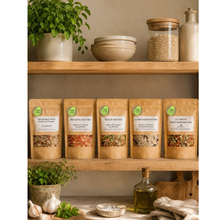 Load image into Gallery viewer, Five stand-up pouches of Mediterranean Flavors seasoning mixes displayed on wooden kitchen shelves alongside potted herbs, bowls, and a glass jar of grains, creating a warm, rustic lifestyle scene.

