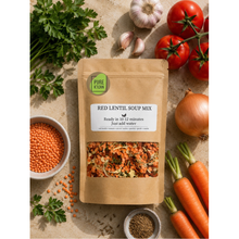 Load image into Gallery viewer, A kraft paper pouch of Pure Kitchen Red Lentil Soup Mix is displayed in a styled flat-lay arrangement with fresh ingredients including carrots, tomatoes, garlic, parsley, and an onion on a textured beige background.
