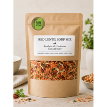 Load image into Gallery viewer, A stand-up kraft paper pouch of Pure Kitchin Red Lentil Soup Mix, featuring a clear window showing the mixed lentils and vegetables inside. The pouch is styled on a light beige surface with a bowl, parsley, and a small dish of lentils in the background.
